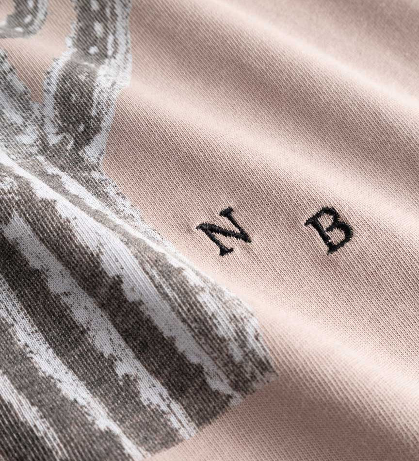 Closeup view of white embroidered NB initials next to cactus print on beige T-shirt