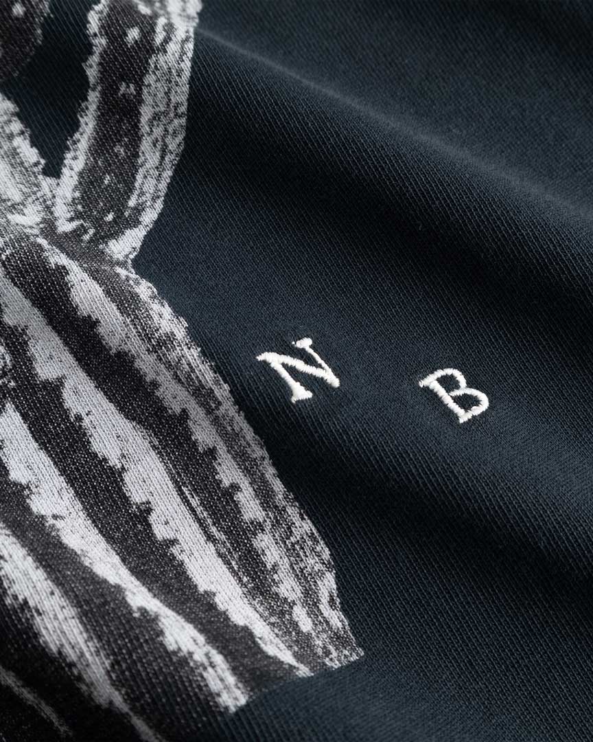 Closeup view of white embroidered NB initials next to cactus print on black T-shirt
