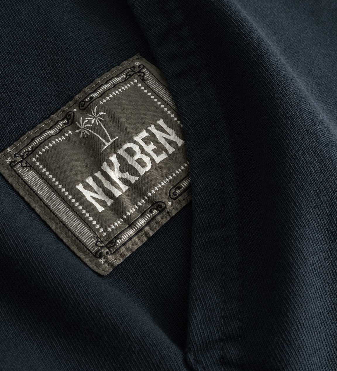 Closeup view of green Nikben patch logo next to left pocket on black hoodie 