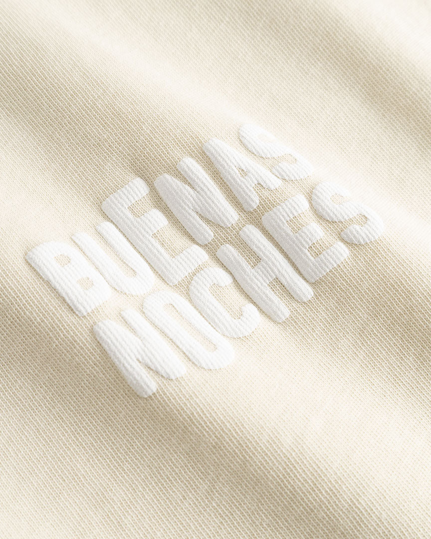 Closeup view of white "BUENAS NOCHES" text print on beige T-shirt