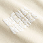 Closeup view of white "BUENAS NOCHES" text print on beige T-shirt