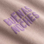 Closeup view of purple "BUENAS NOCHES" text print on brown T-shirt