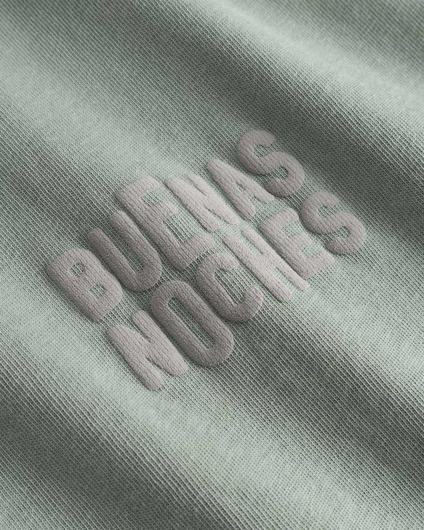 Closeup view of brown "BUENAS NOCHES" text print on green T-shirt
