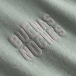 Closeup view of brown "BUENAS NOCHES" text print on green T-shirt
