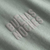 Closeup view of brown "BUENAS NOCHES" text print on green T-shirt