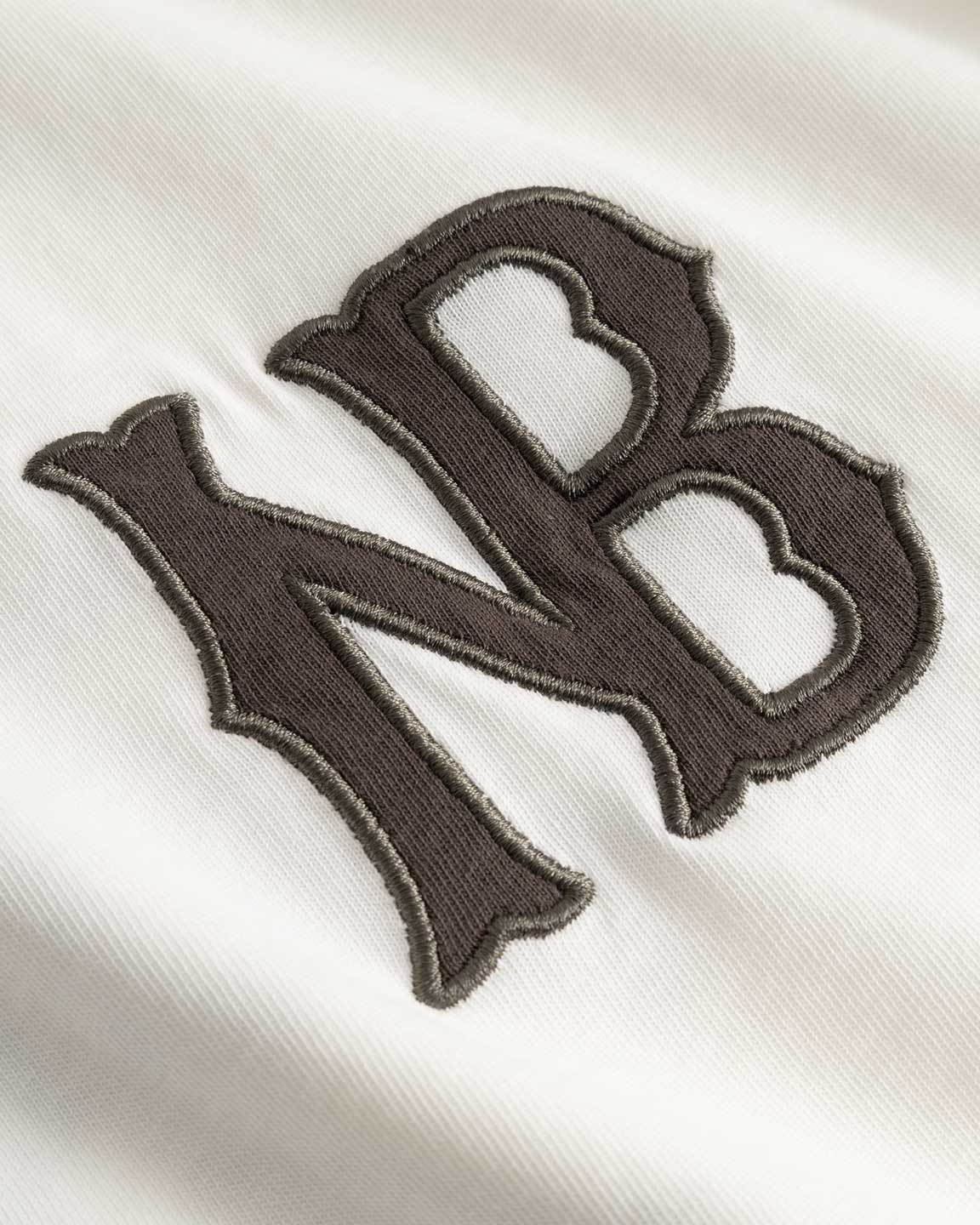 Closeup view of brown NB logo on white longsleeve T-shirt