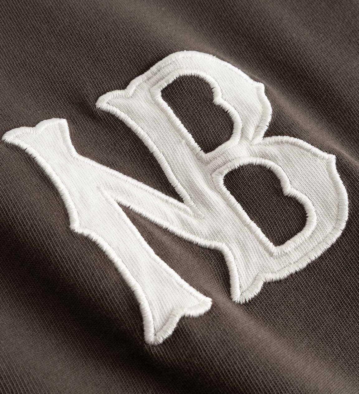 Closeup view of white NB logo on brown longsleeve T-shirt