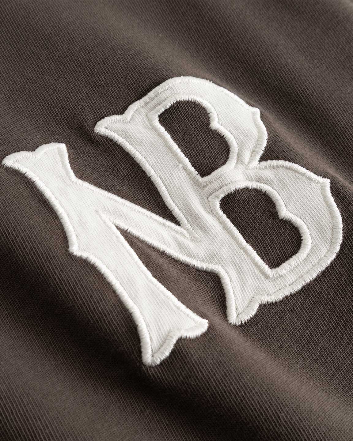 Closeup view of white NB logo on brown longsleeve T-shirt