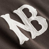 Closeup view of white NB logo on brown longsleeve T-shirt