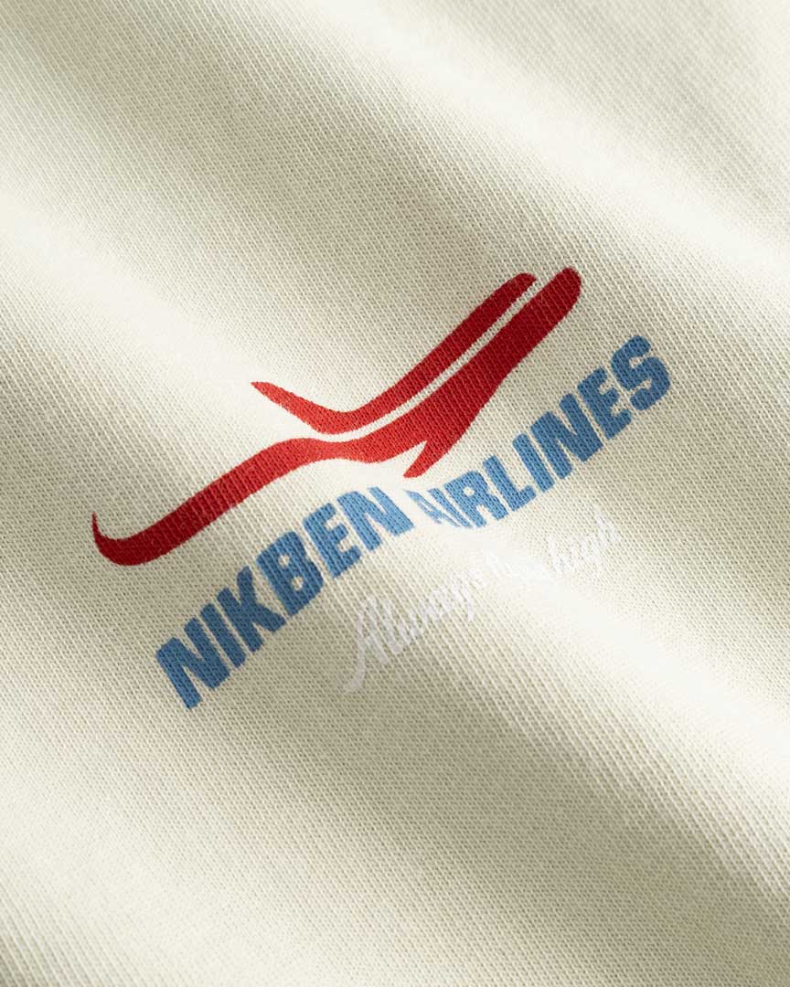 Closeup view of blue Nikben Airlines logo and red airplane print on light grey T-shirt