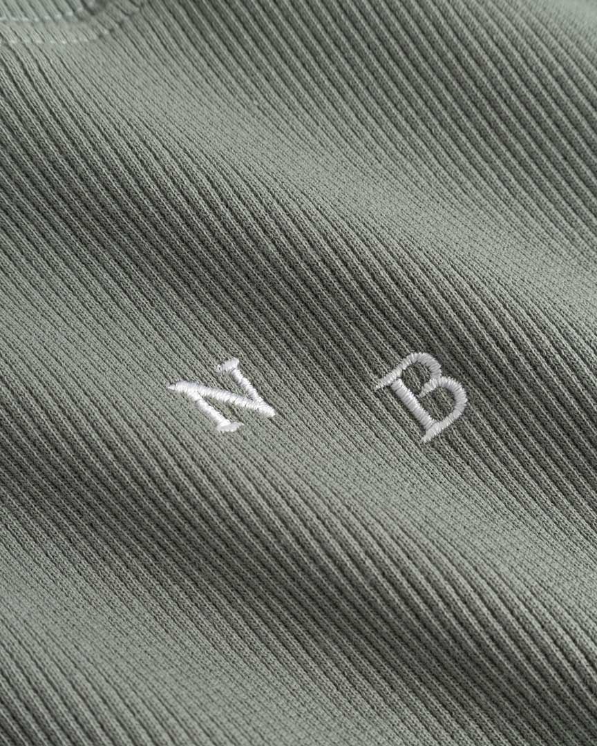 Closeup view of white NB initials on green ribbed tank top