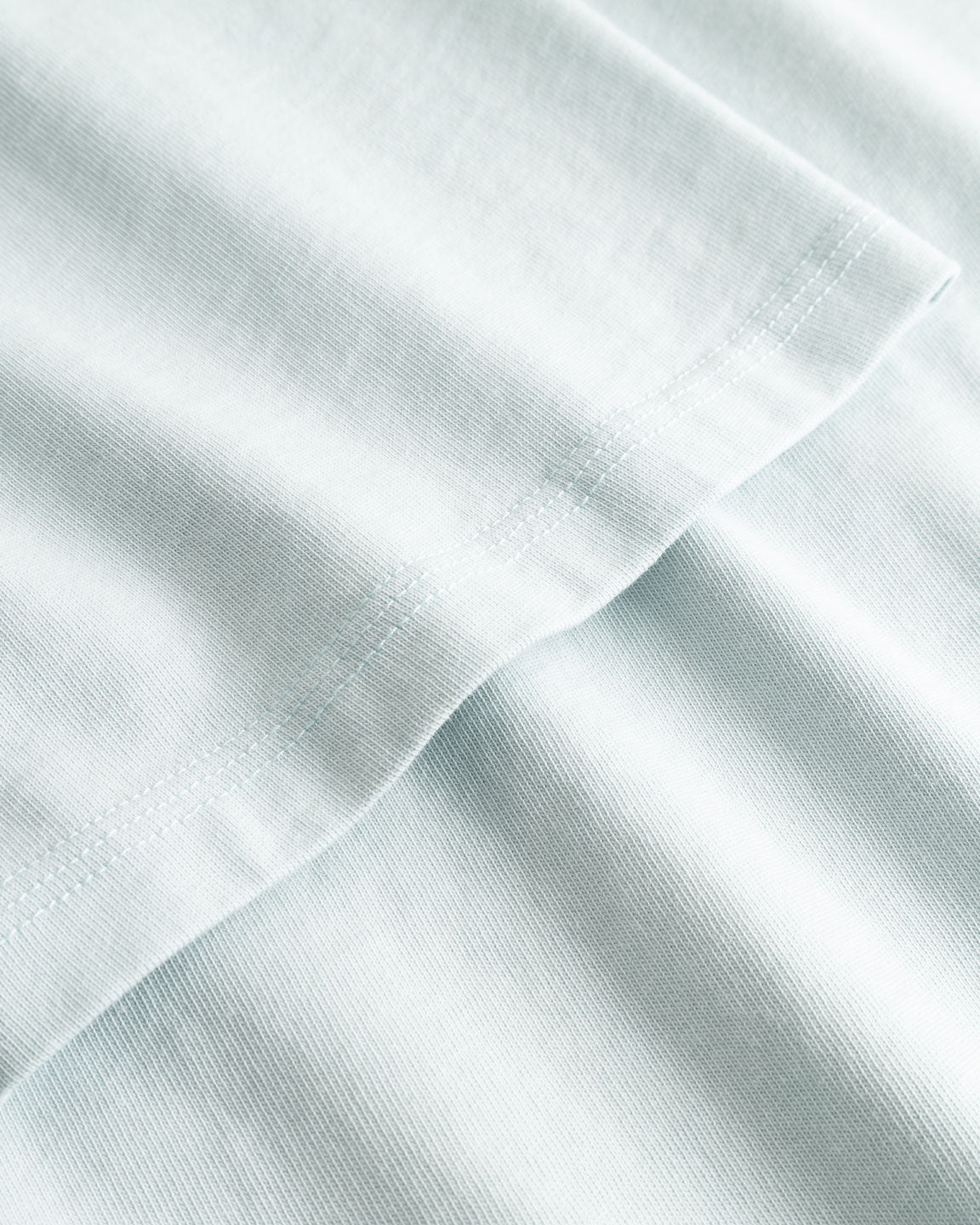 Closeup view of arm stitchings on pale blue T-shirt