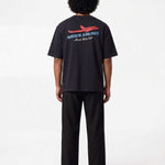 Back of male model wearing black T-shirt with blue Nikben Airlines logo and red airplane print 