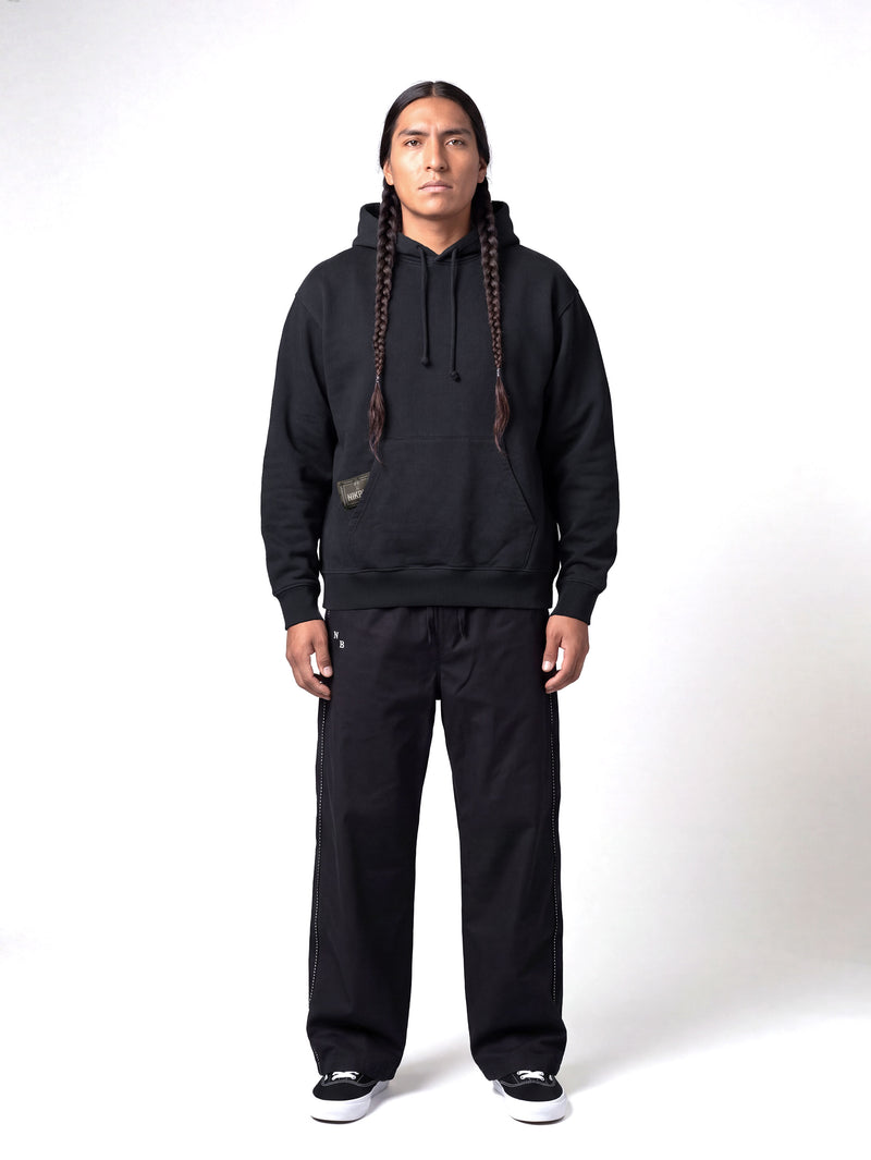 Male model wearing black hoodie with green Nikben patch label next to left pocket 