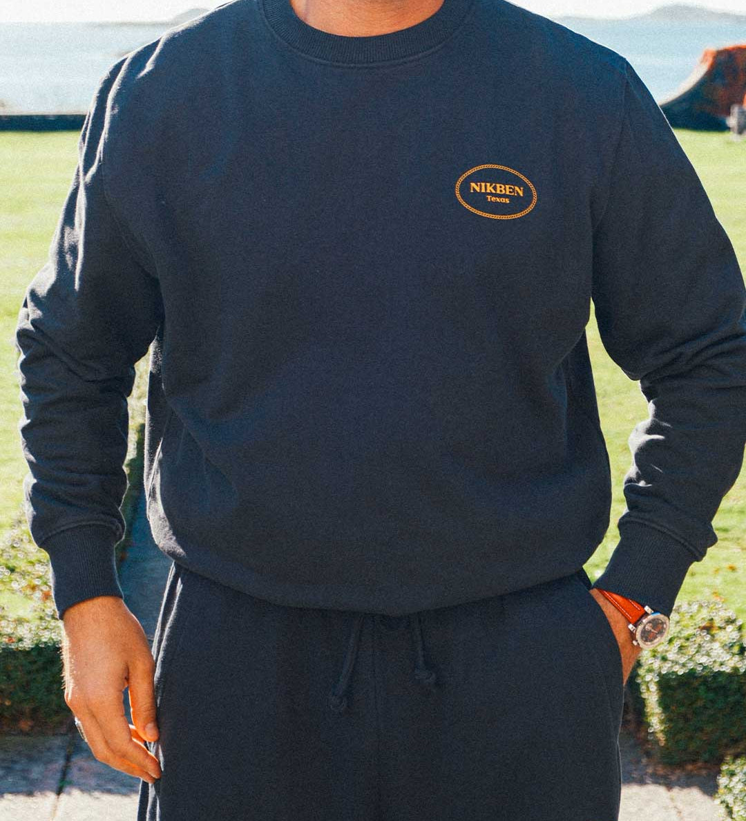 Model wearing a complete black tracksuit with draw string and logo on front breast and lower leg