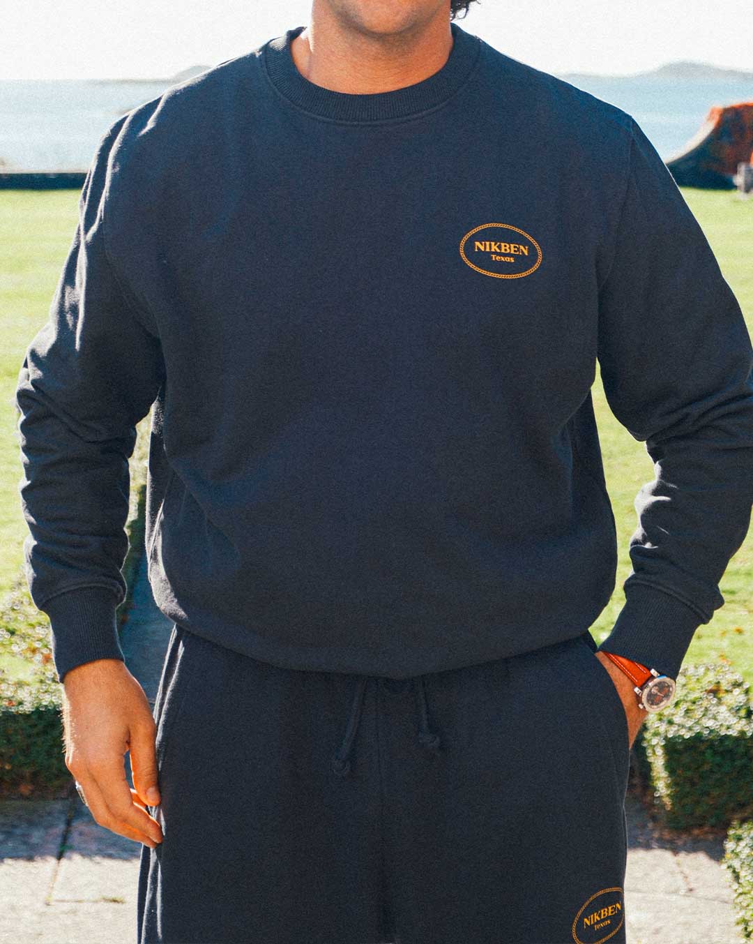 Model wearing a complete black tracksuit with draw string and logo on front breast and lower leg