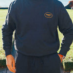 Model wearing a complete black tracksuit with draw string and logo on front breast and lower leg