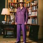 Model wearing a purple outfit standing in a room with bookshelves and decorative items.