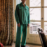 Model is wearing a green outfit standing in a room with a large window and patterned curtain.