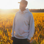 Model wearing a beige hoodie standing in a field with sunset light