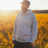 Model wearing a beige hoodie standing in a field with sunset light