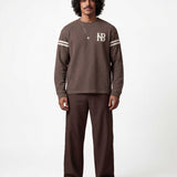 Male model wearing brown longsleeve T-shirt with white NB logo on chest and white stripes on sleeves