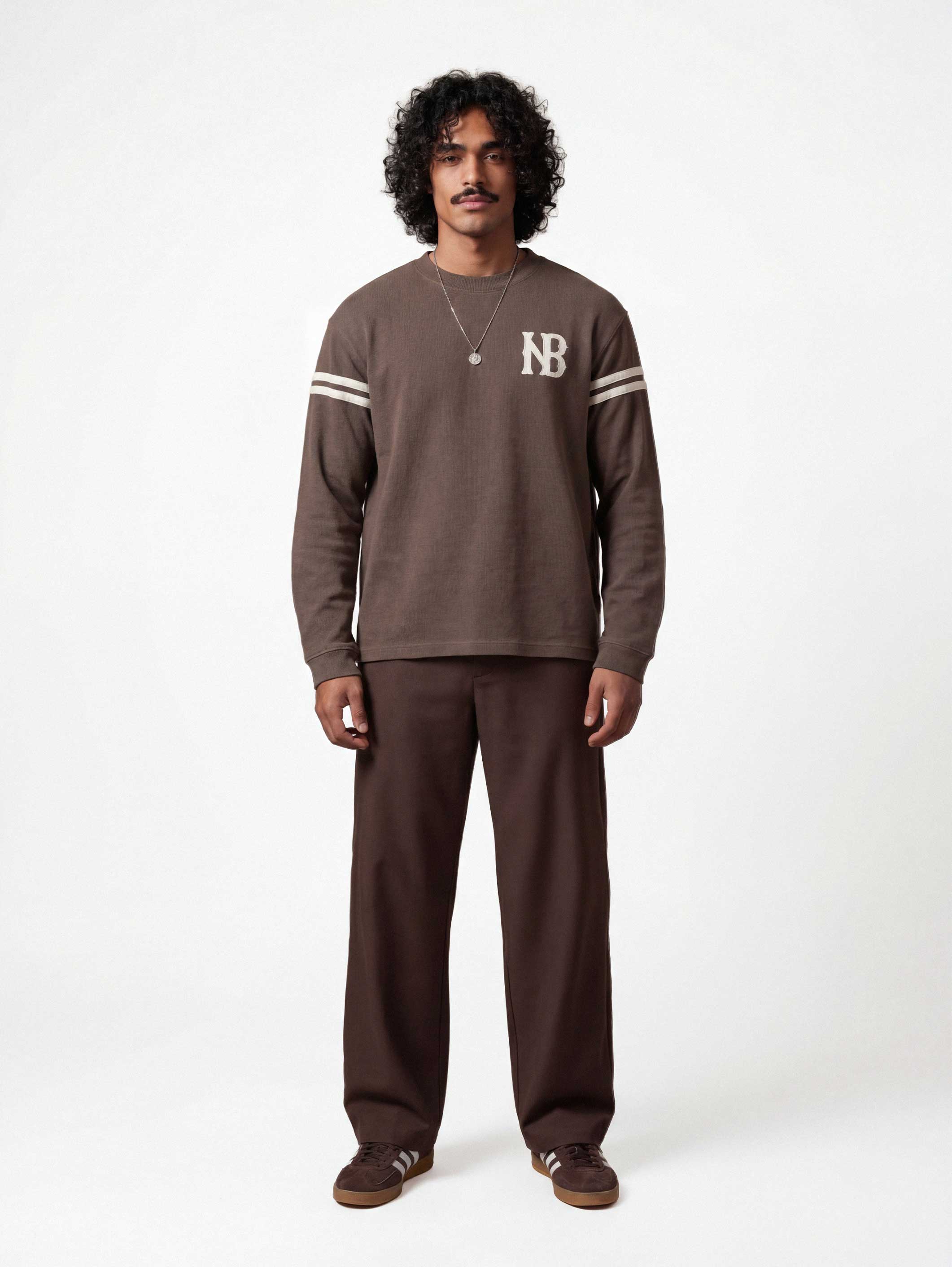 Male model wearing brown longsleeve T-shirt with white NB logo on chest and white stripes on sleeves