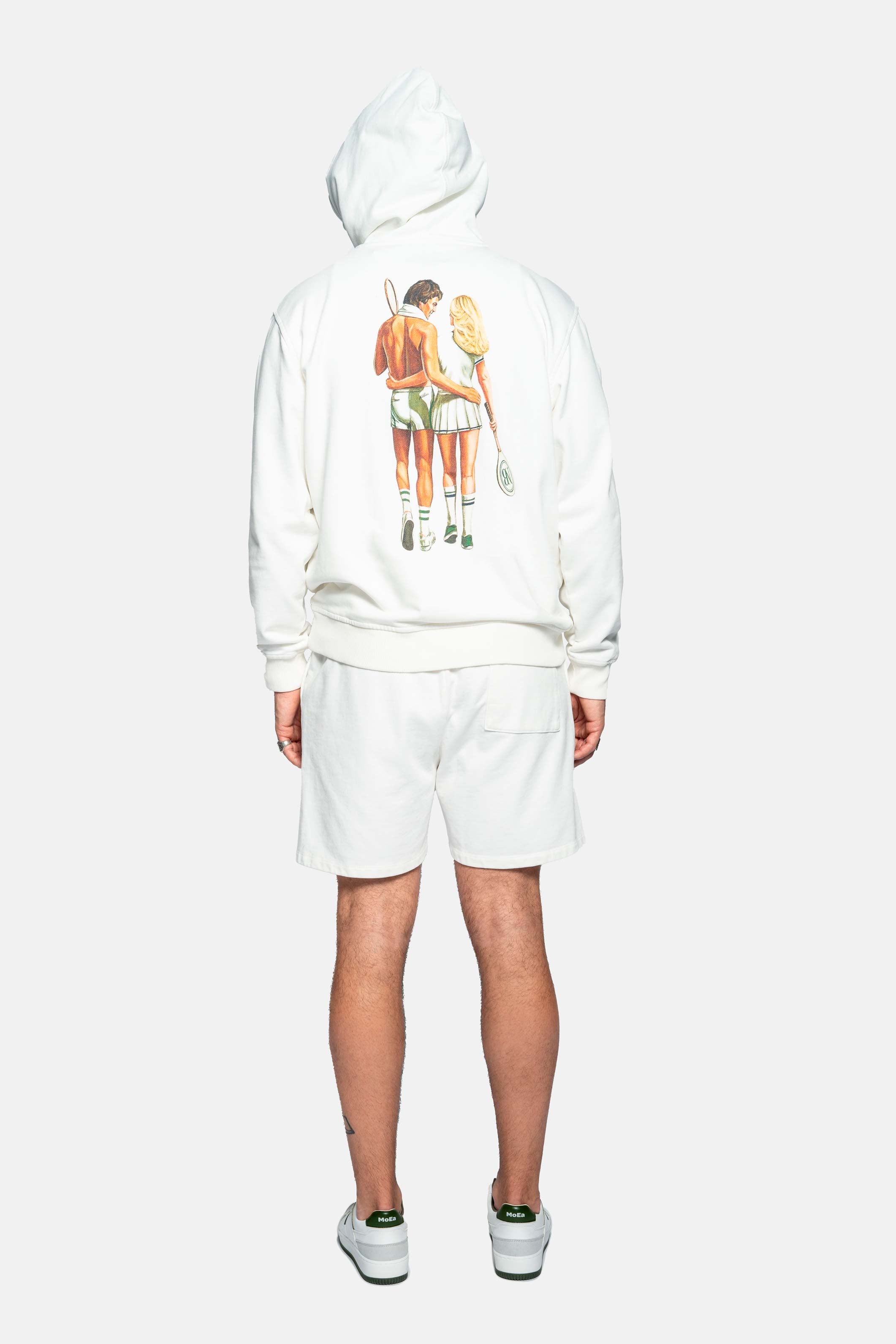 Back of male model wearing a cream colored hoodie with male and female tennis player back print 