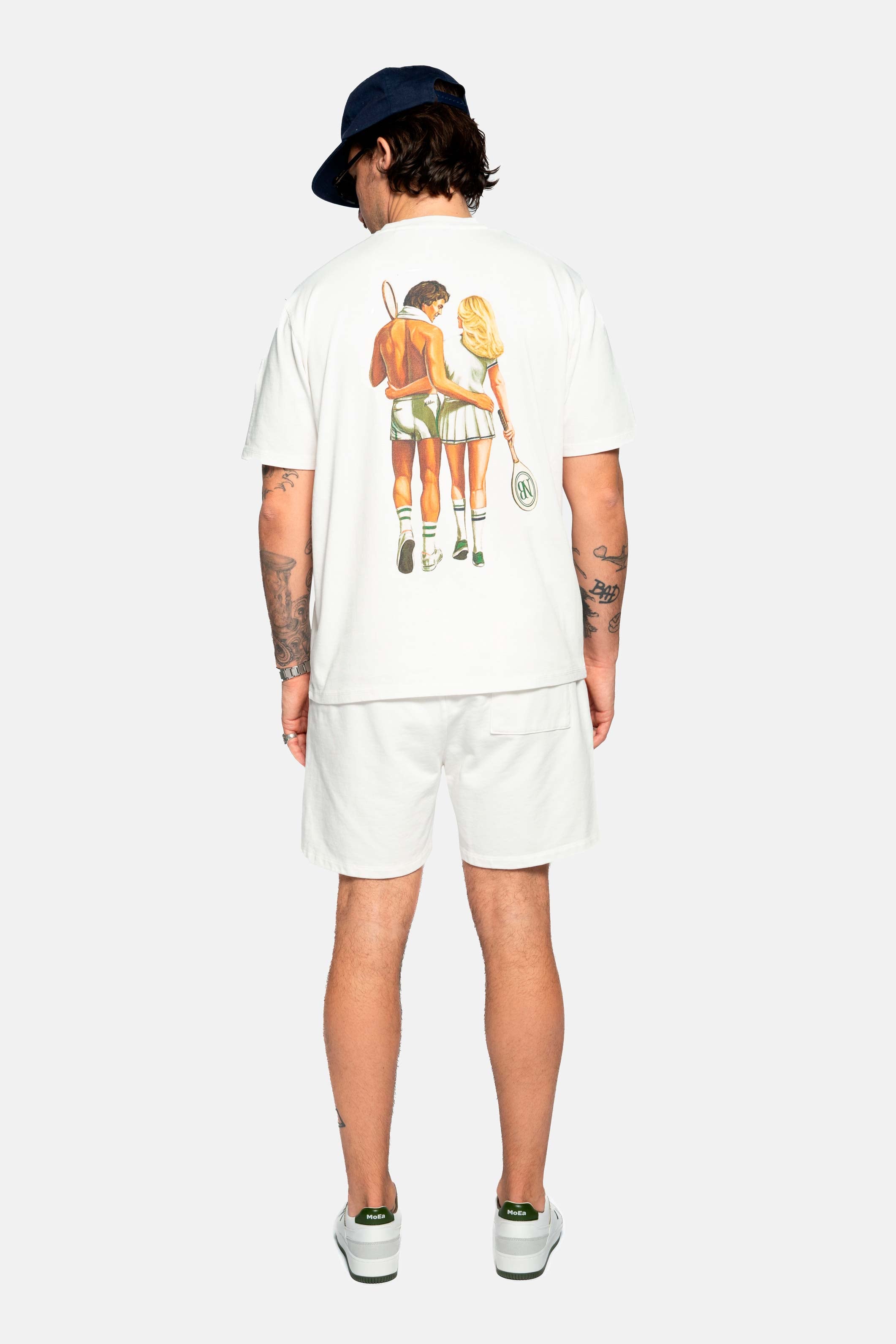 Back of male model wearing a cream colored t-shirt with male and female tennis players back print 