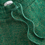Close-up of a green textured fabric with a brand label, featuring a herringbone pattern.