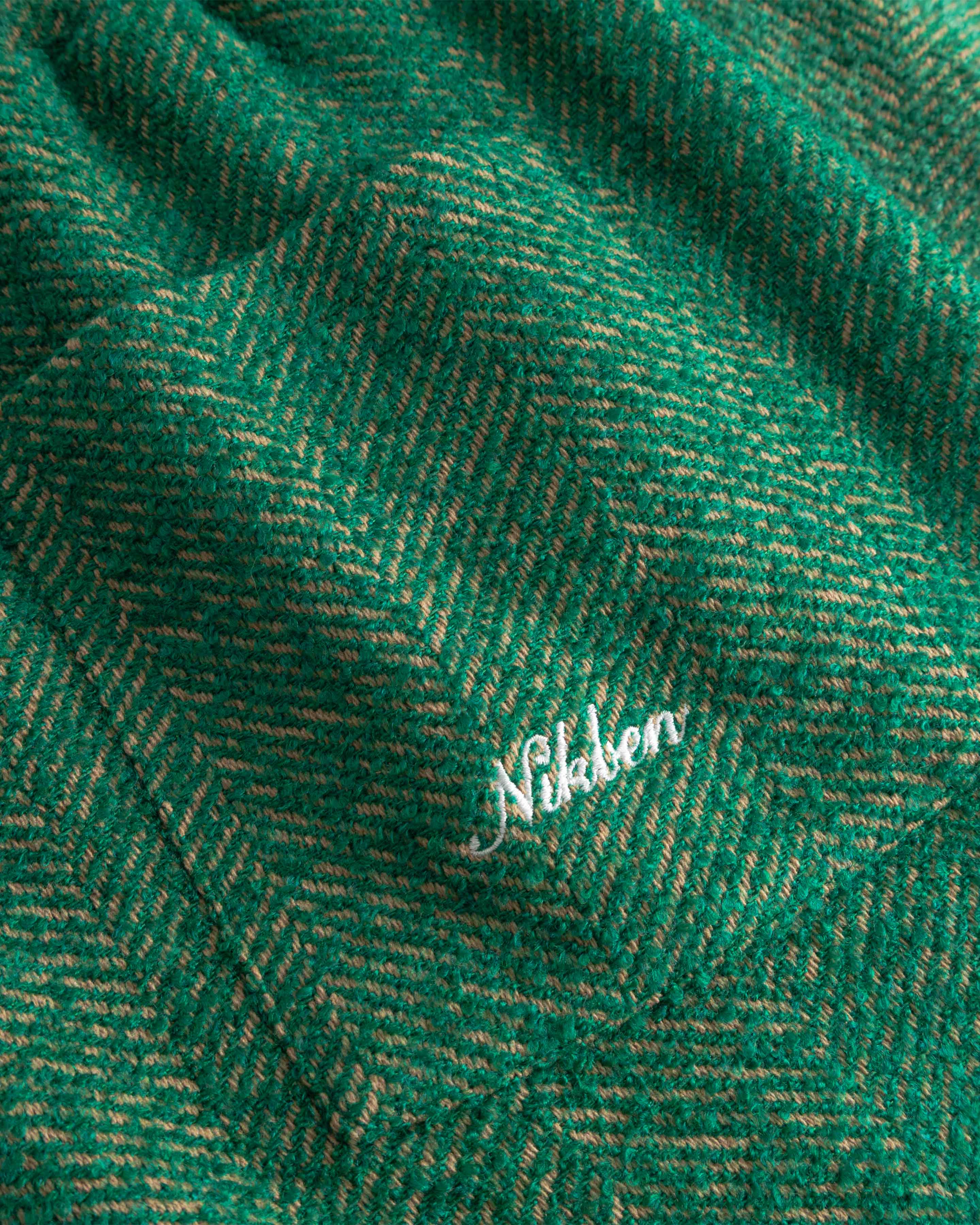 Close-up of green fabric with a subtle pattern and 'Nikben' brand logo.