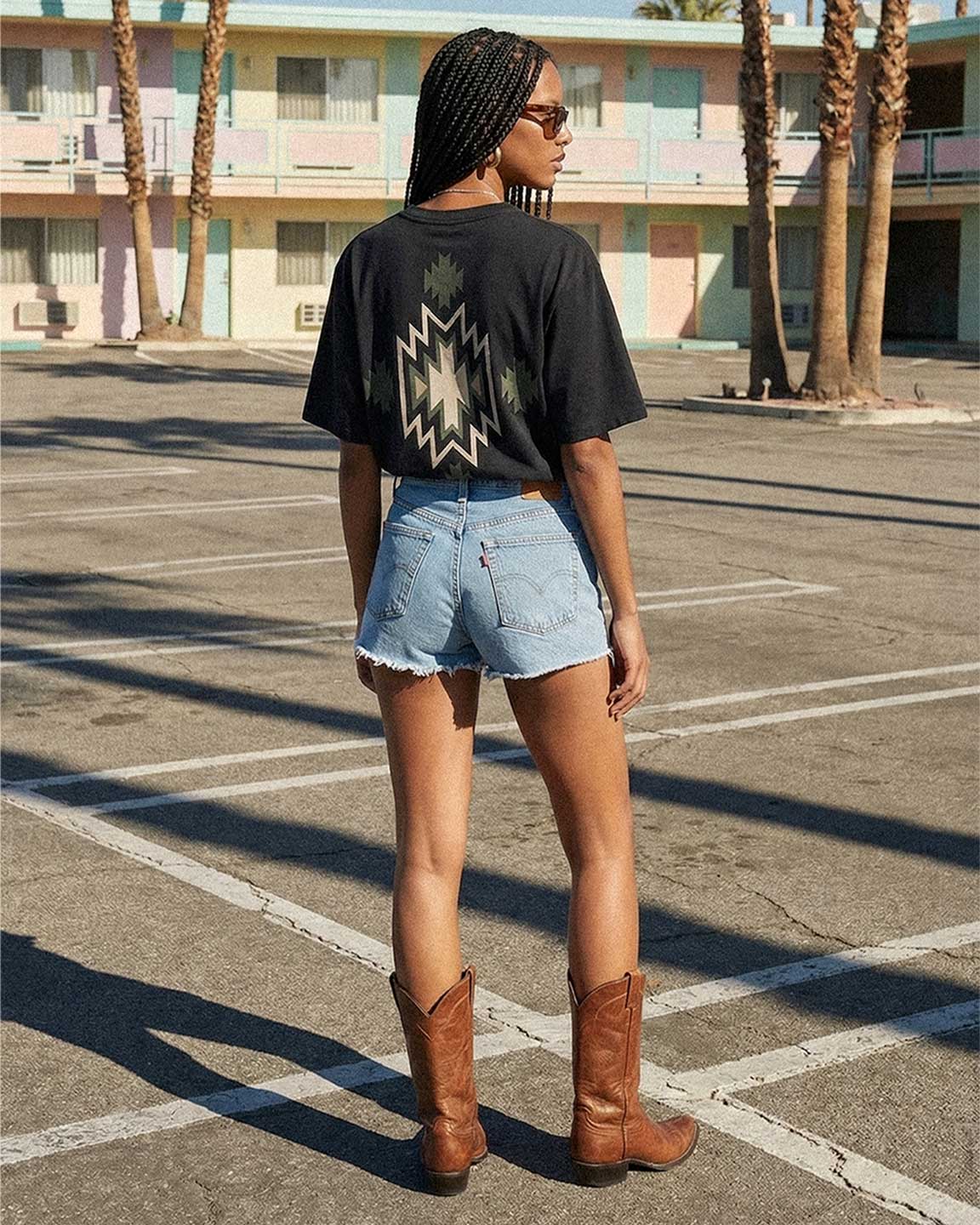 Back of female model wearing black T-shirt with native inspired backprint in green, white and black