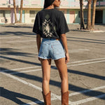 Back of female model wearing black T-shirt with native inspired backprint in green, white and black