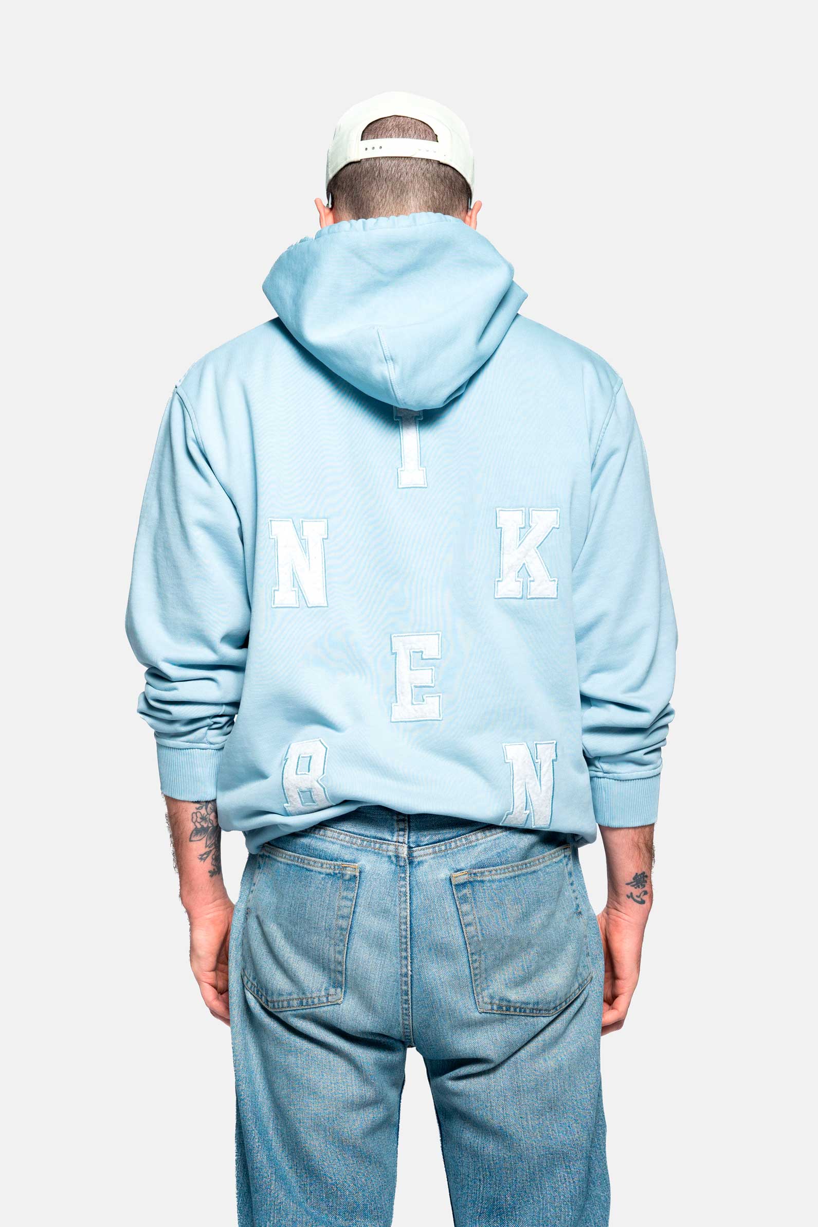 Back of male model wearing a baby blue hoodie with embroidered Nikben letters