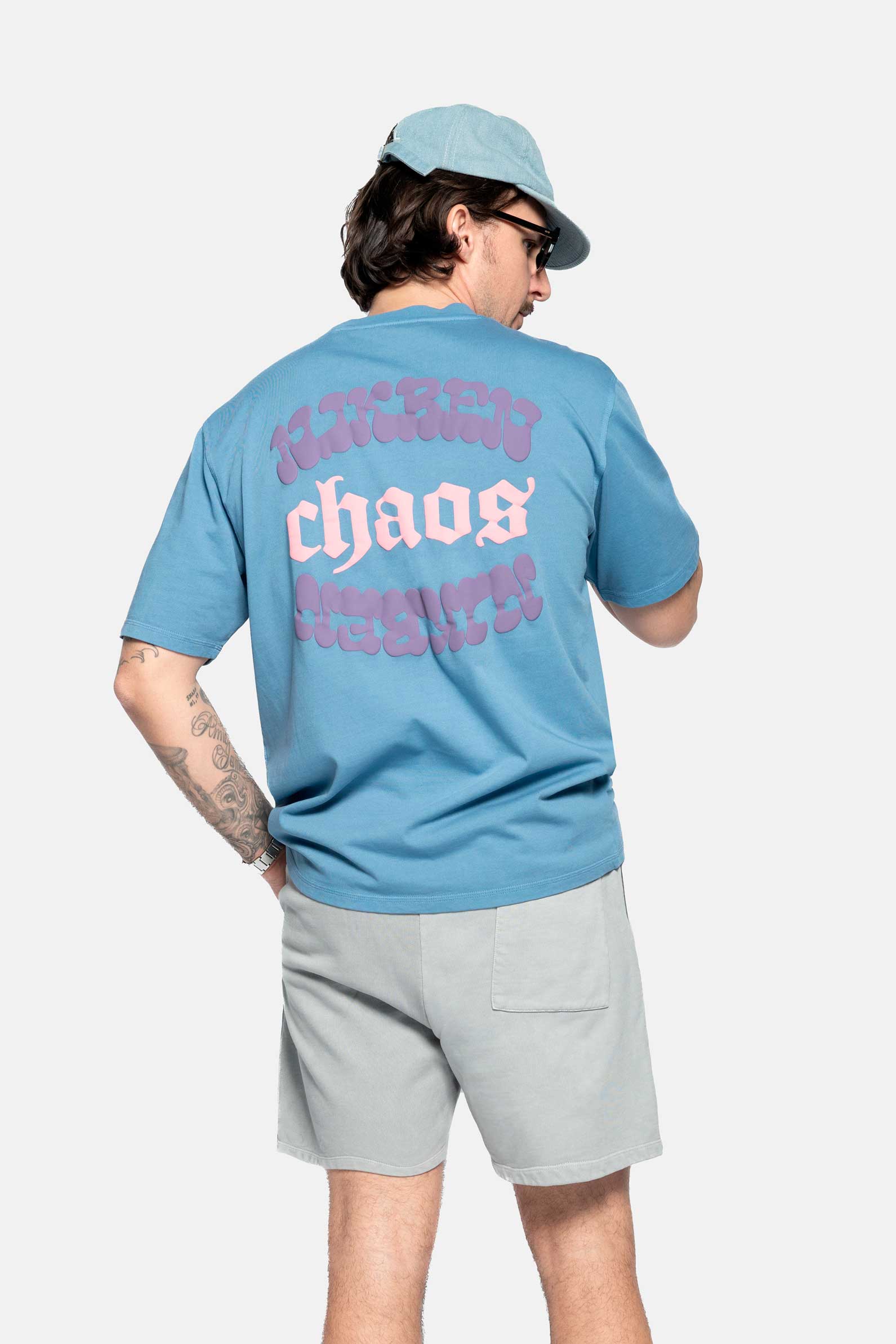 back of male model wearing a blue t-shirt with pink and purple back print