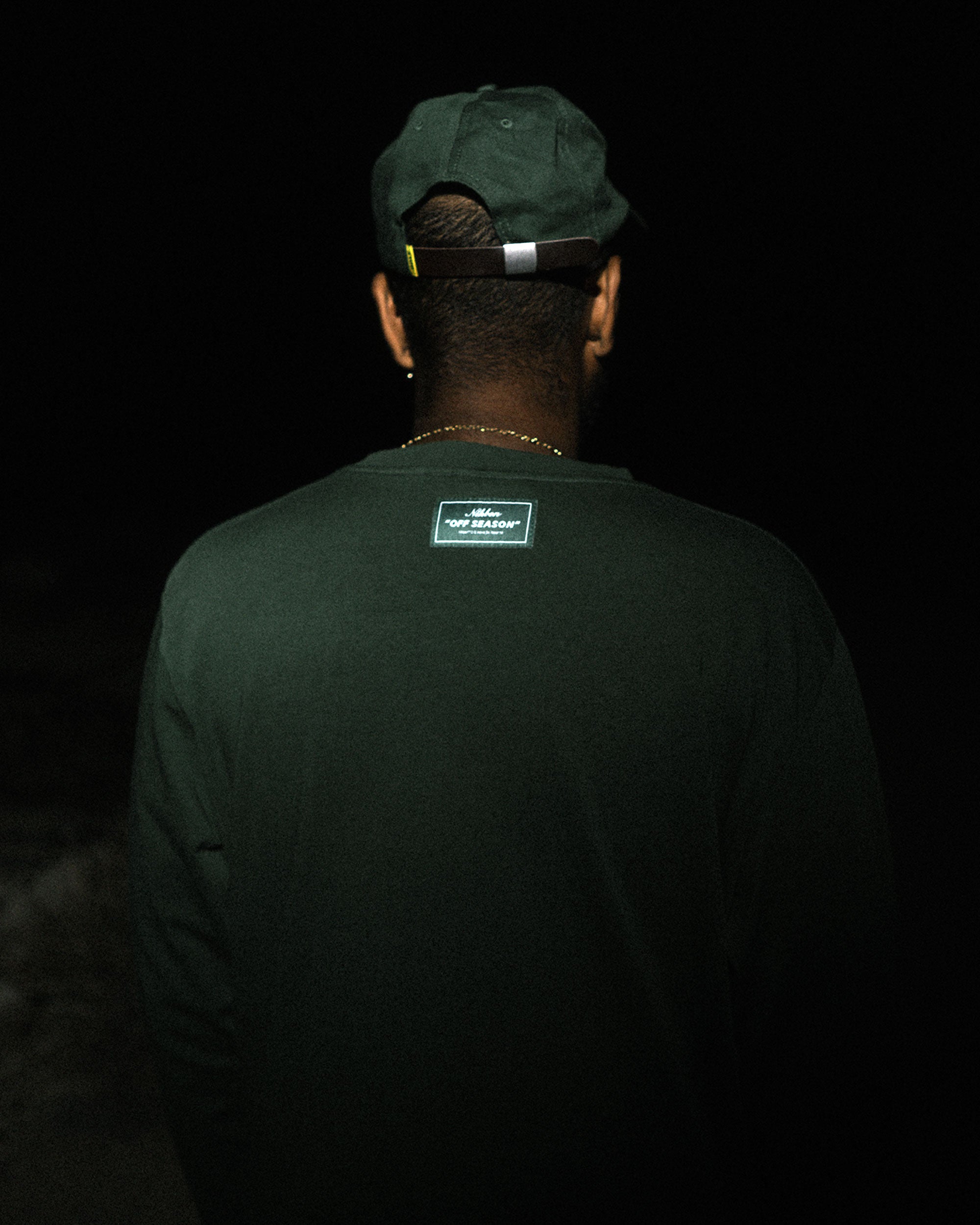 Back view of male model wearing a green long-sleeved t-shirt with a patch in the neck.