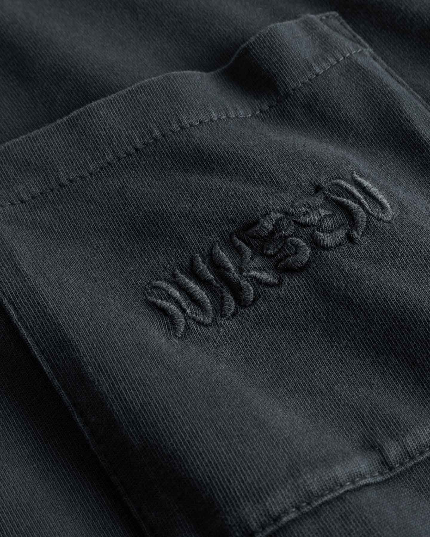 Close-up of chest pocket with tone in tone embroidered "nikben" logo on washed black T-shirt