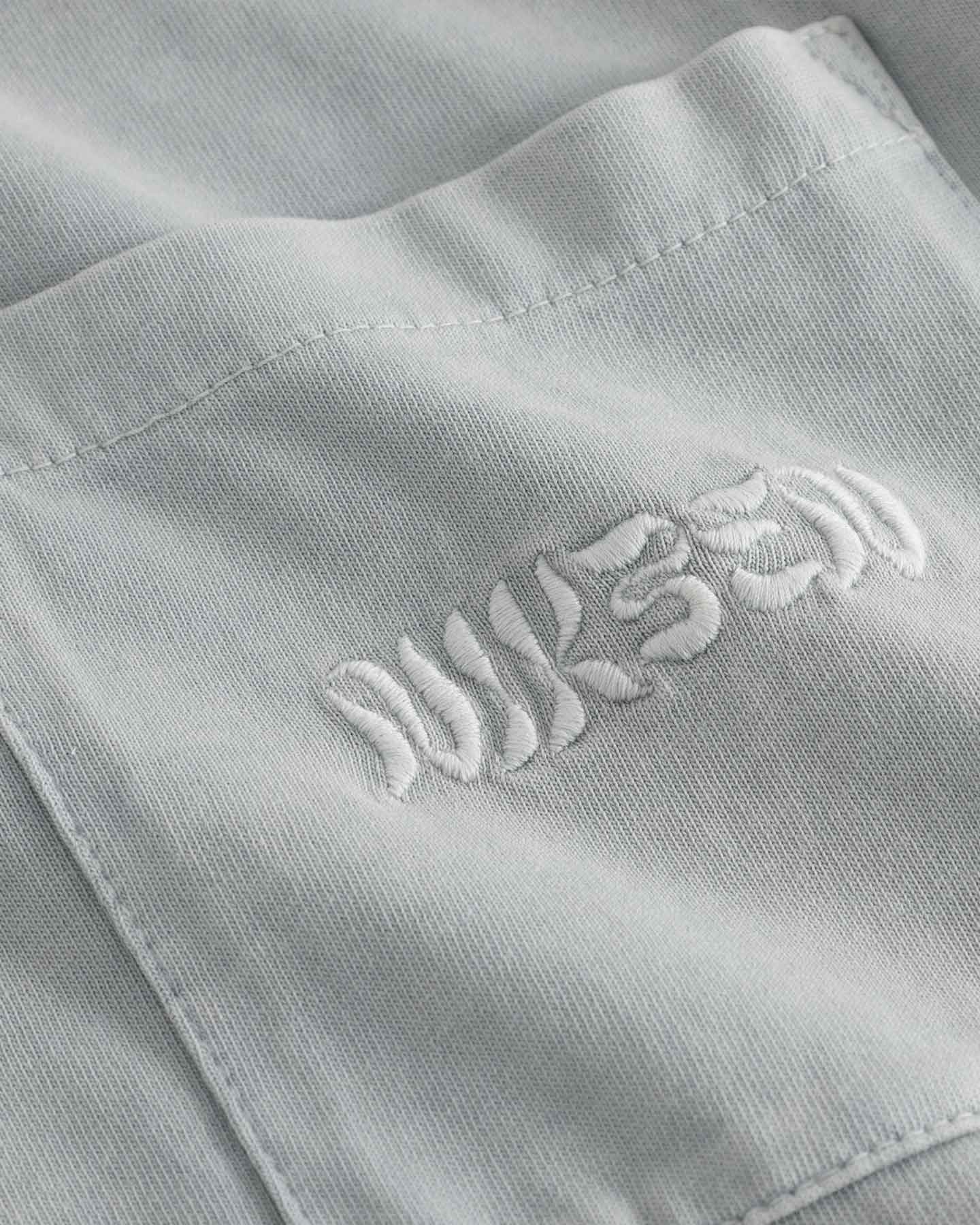 Close up of chest pocket with tone in tone embroidered logo on washed grey t-shirt.