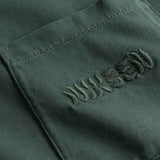 Close up of chest pocket with tone in tone embroidered logo on washed green t-shirt.