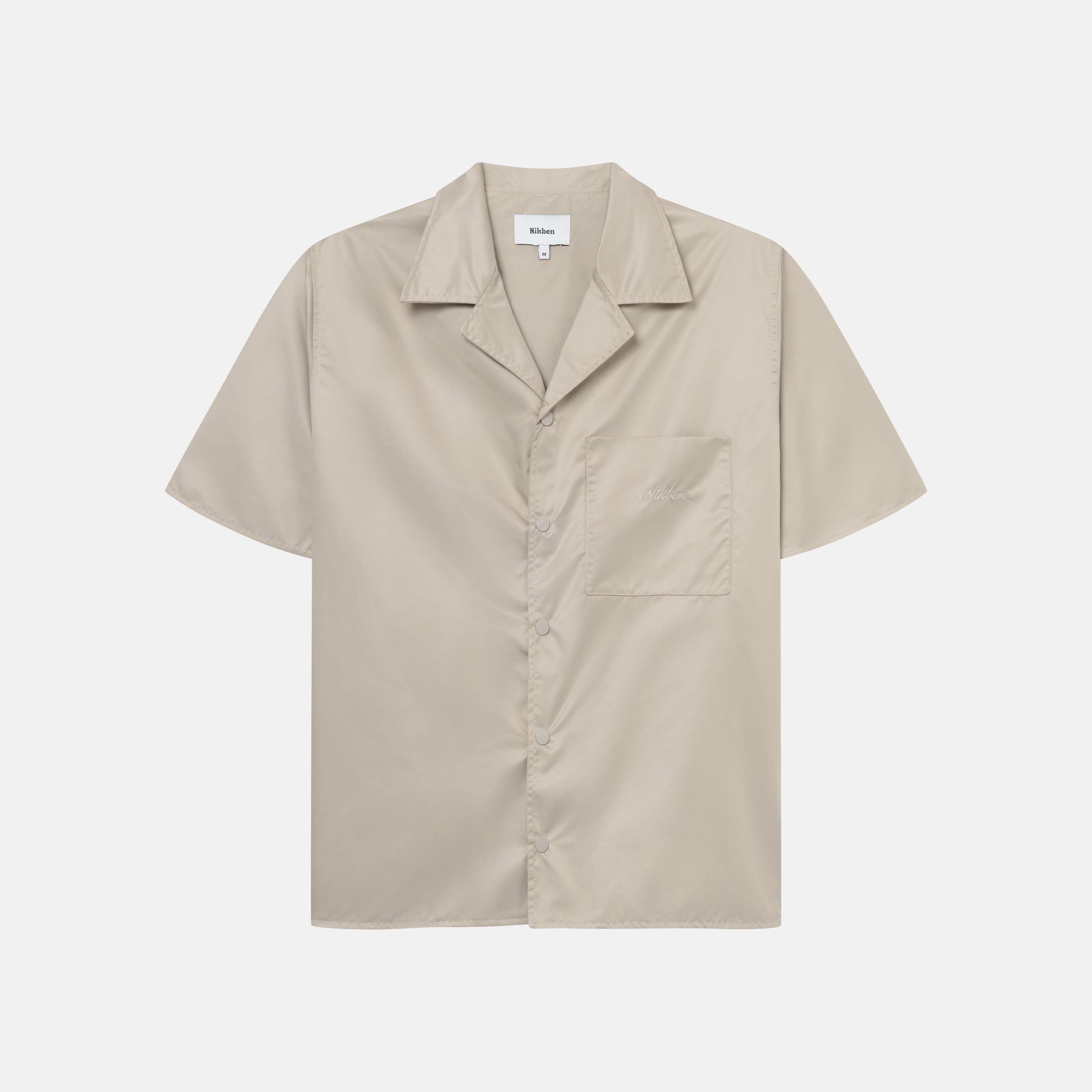 A beige short-sleeved shirt with snap button closure and embroidered Nikben logo on the breast pocket