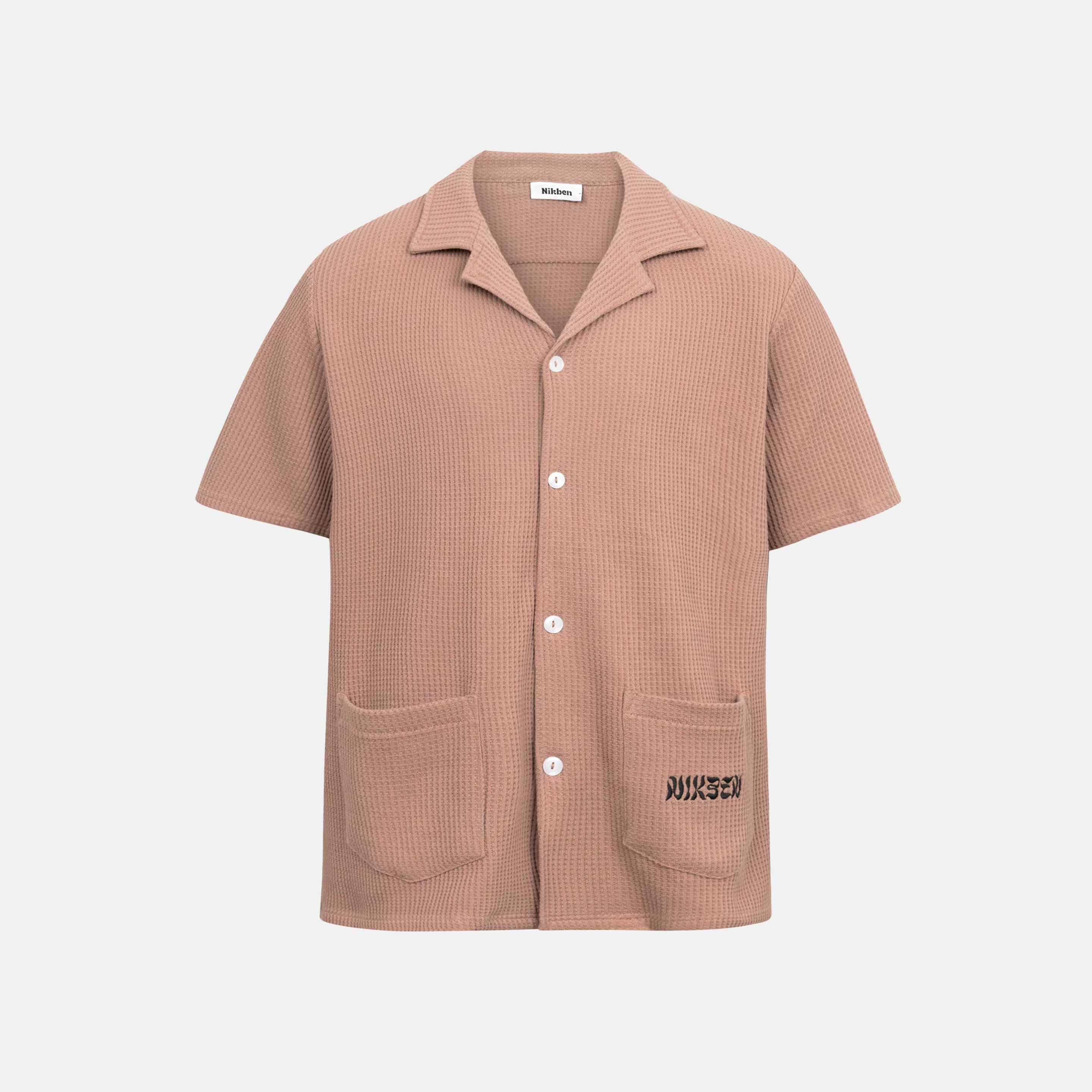Brown waffle-patterned short-sleeved shirt with two front pockets, featuring a stitched black Nikben logo on the left pocket and button closure.