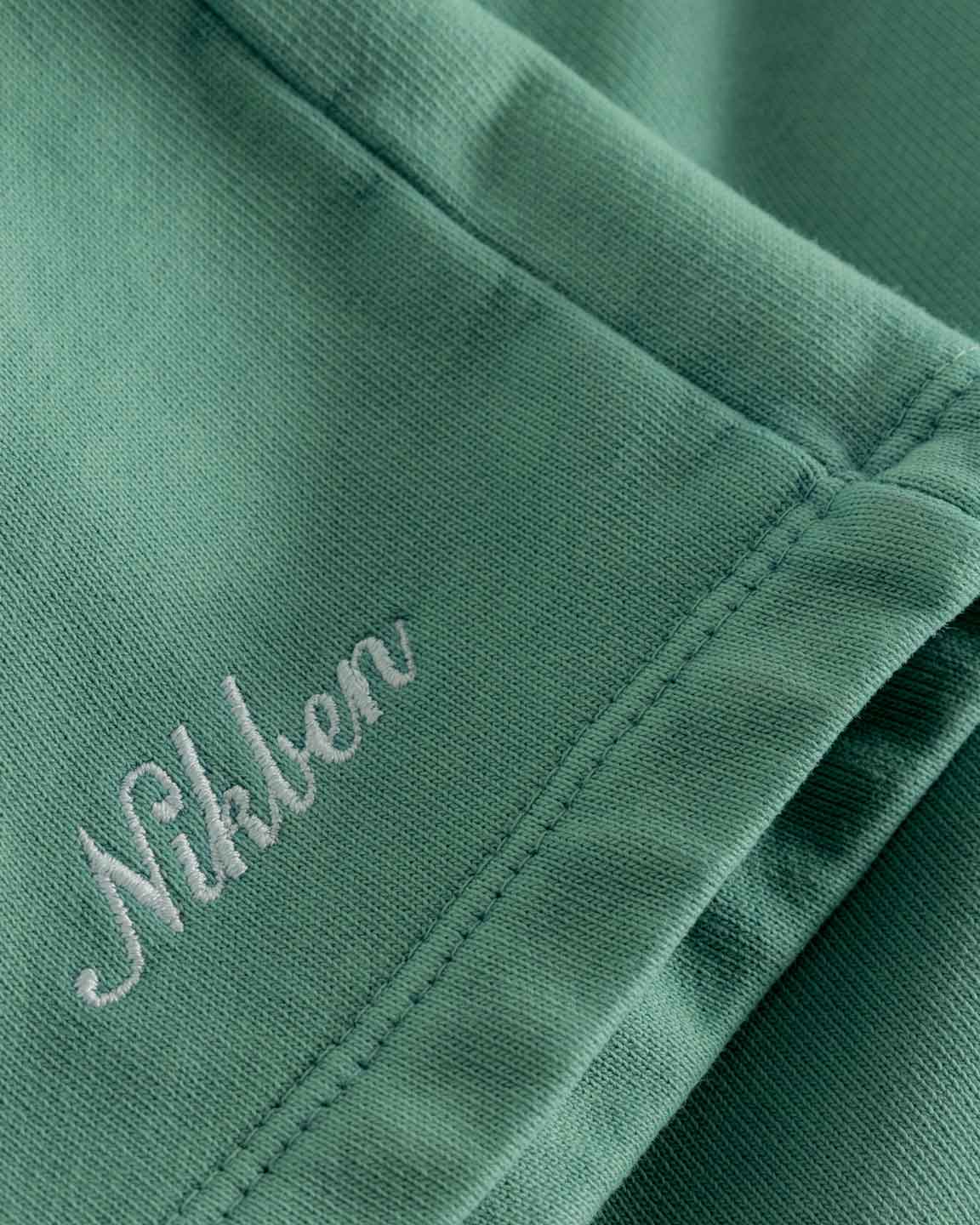 Close up on embroidered script logo on front leg of green sweatshorts