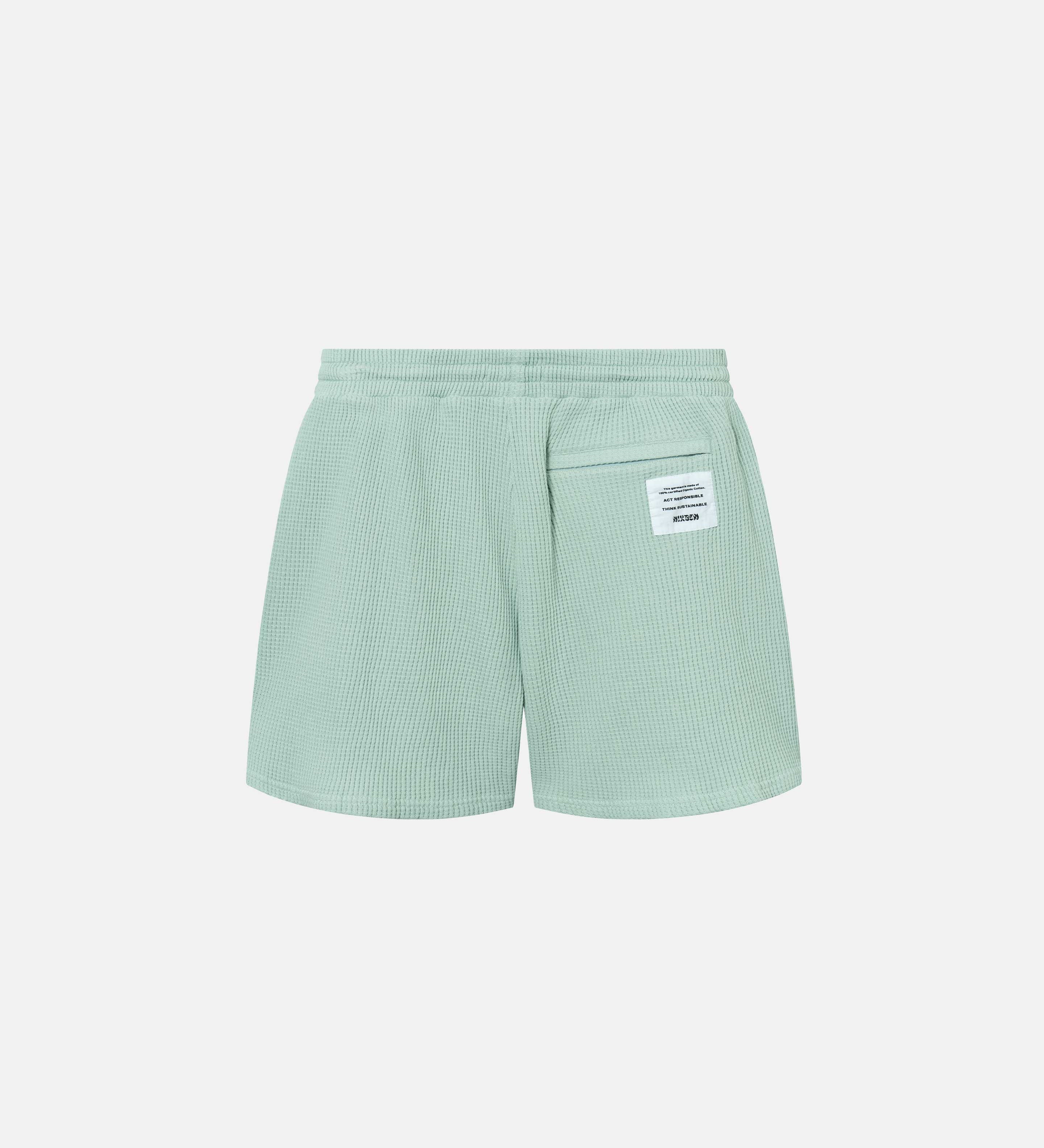 Backside of mint green waffle-patterned mid-length shorts with tone back pocket and logo patch.