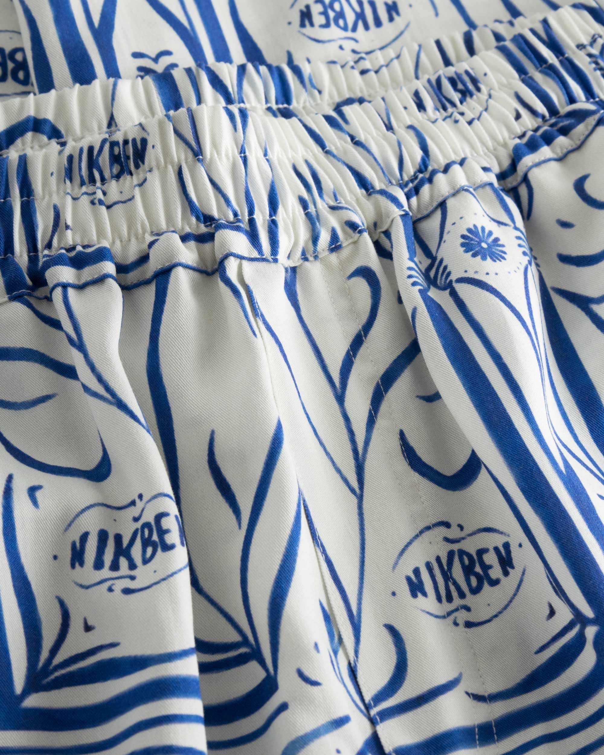 Close up of elastic waistband and blue graphic pattern on white vacation pants.