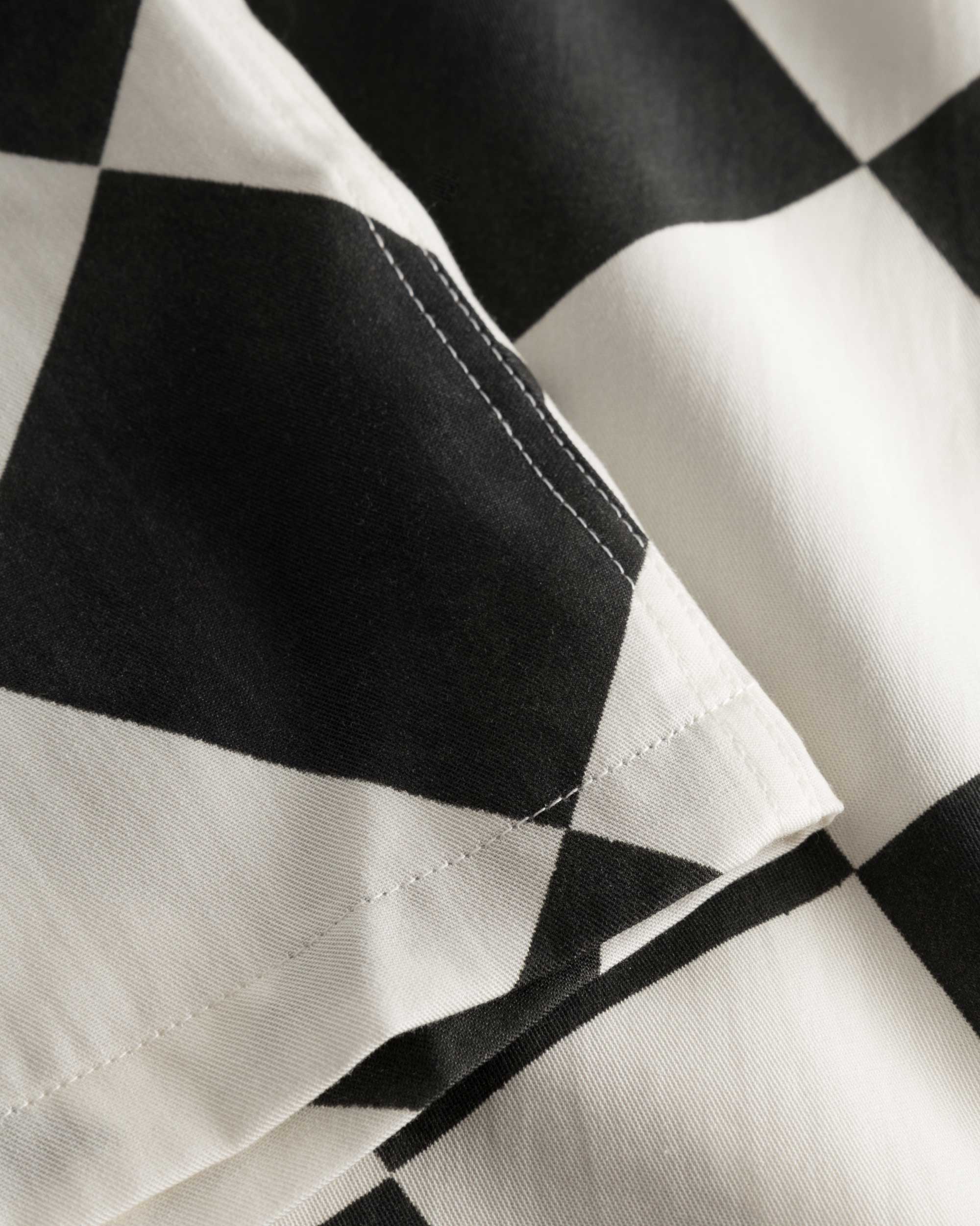Close-up of stitchings and checkered pattern on a black and white vacation shirt.