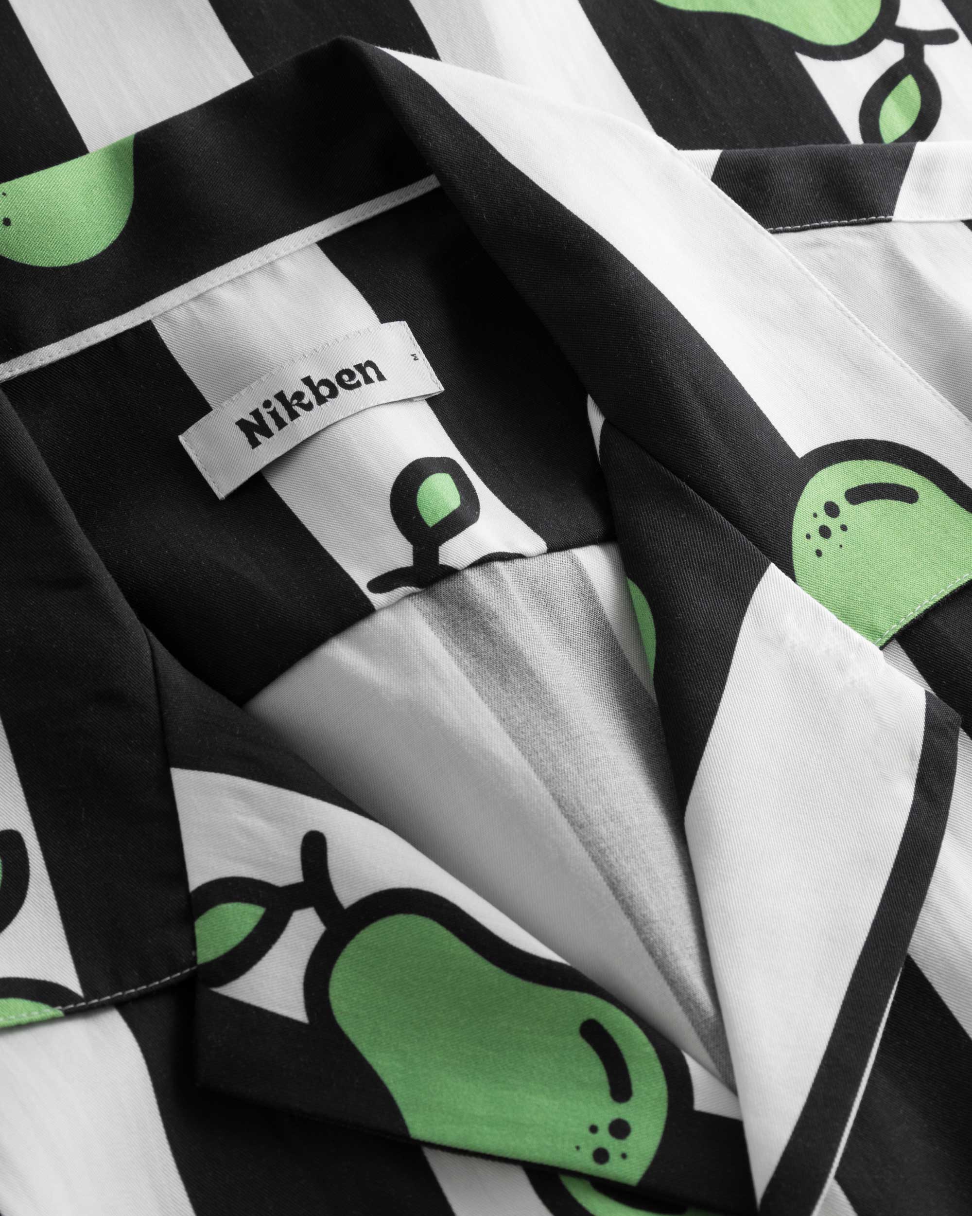 Close-up on open collar on a black and white short-sleeved vacation shirt with green pear illustrations.