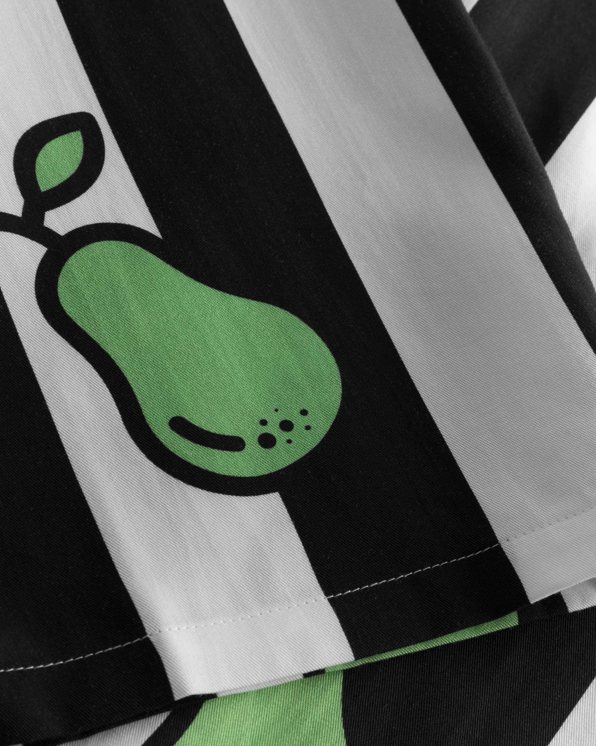 Close-up on stitchings on a black and white short-sleeved vacation shirt with green pear illustrations.