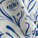 Close-up of the stitchings on a white short-sleeved vacation shirt with blue graphic pattern.