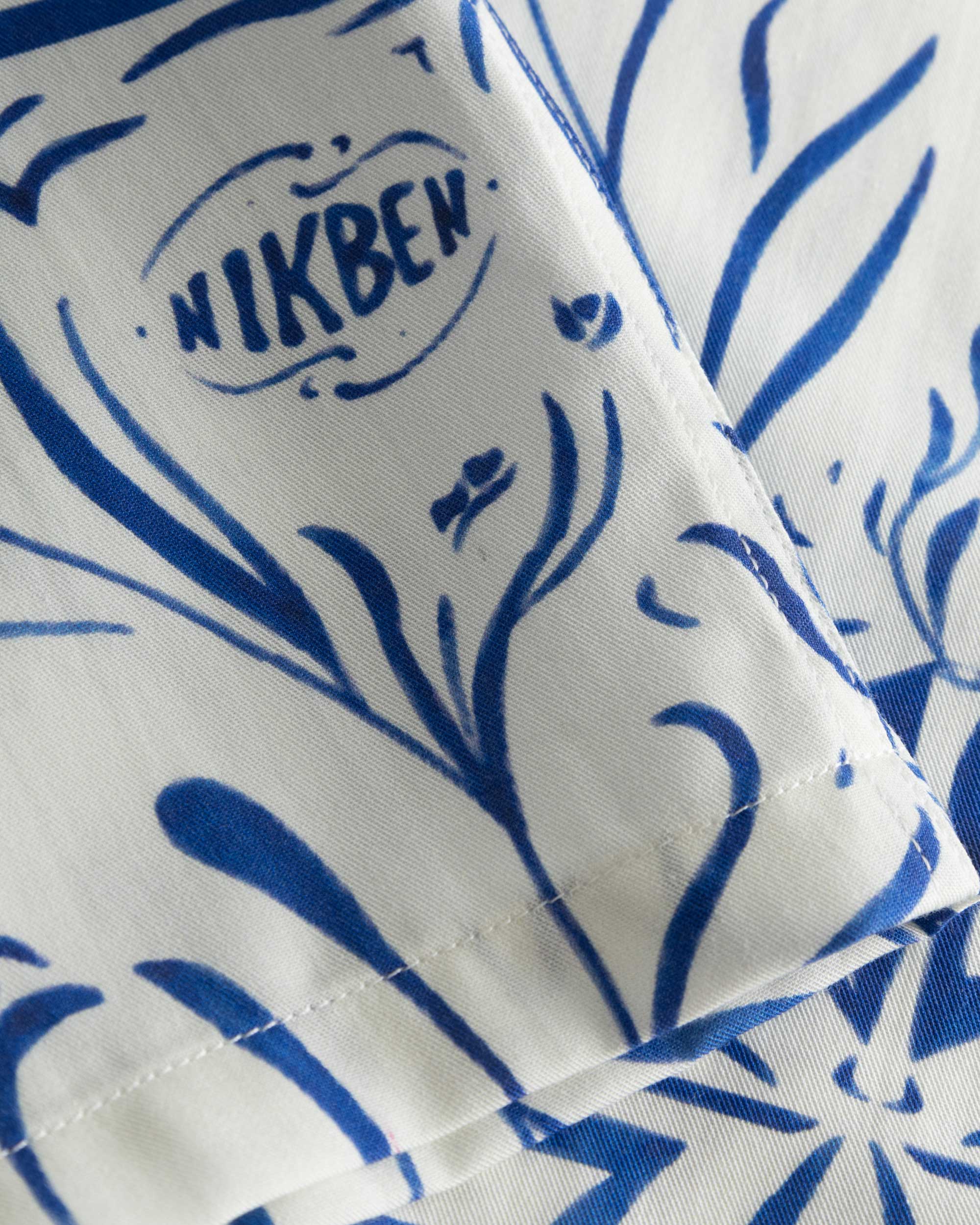 Close-up of the stitchings on a white short-sleeved vacation shirt with blue graphic pattern.