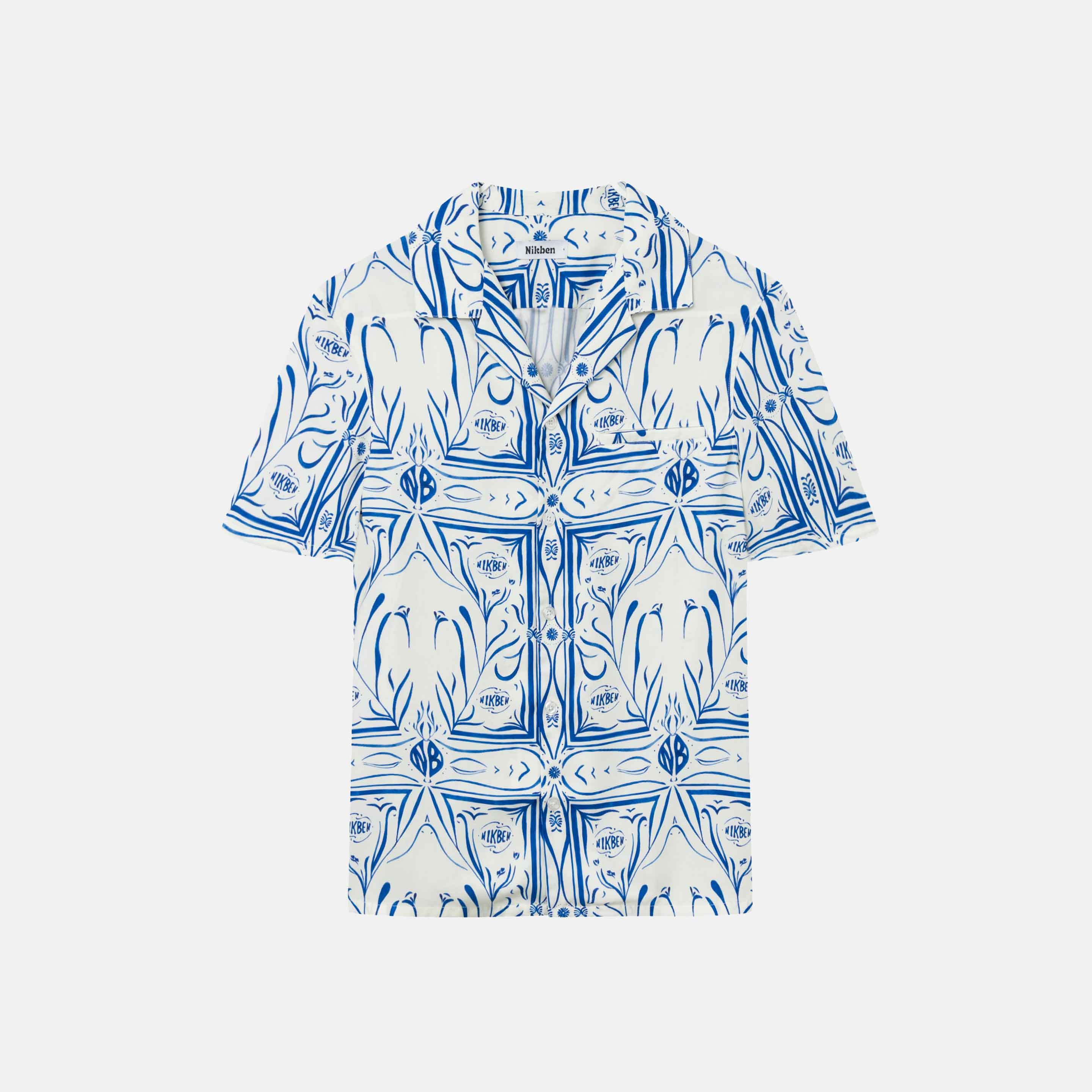 White short-sleeved vacation shirt with blue graphic pattern, open collar, one breast pocket, and button closure.